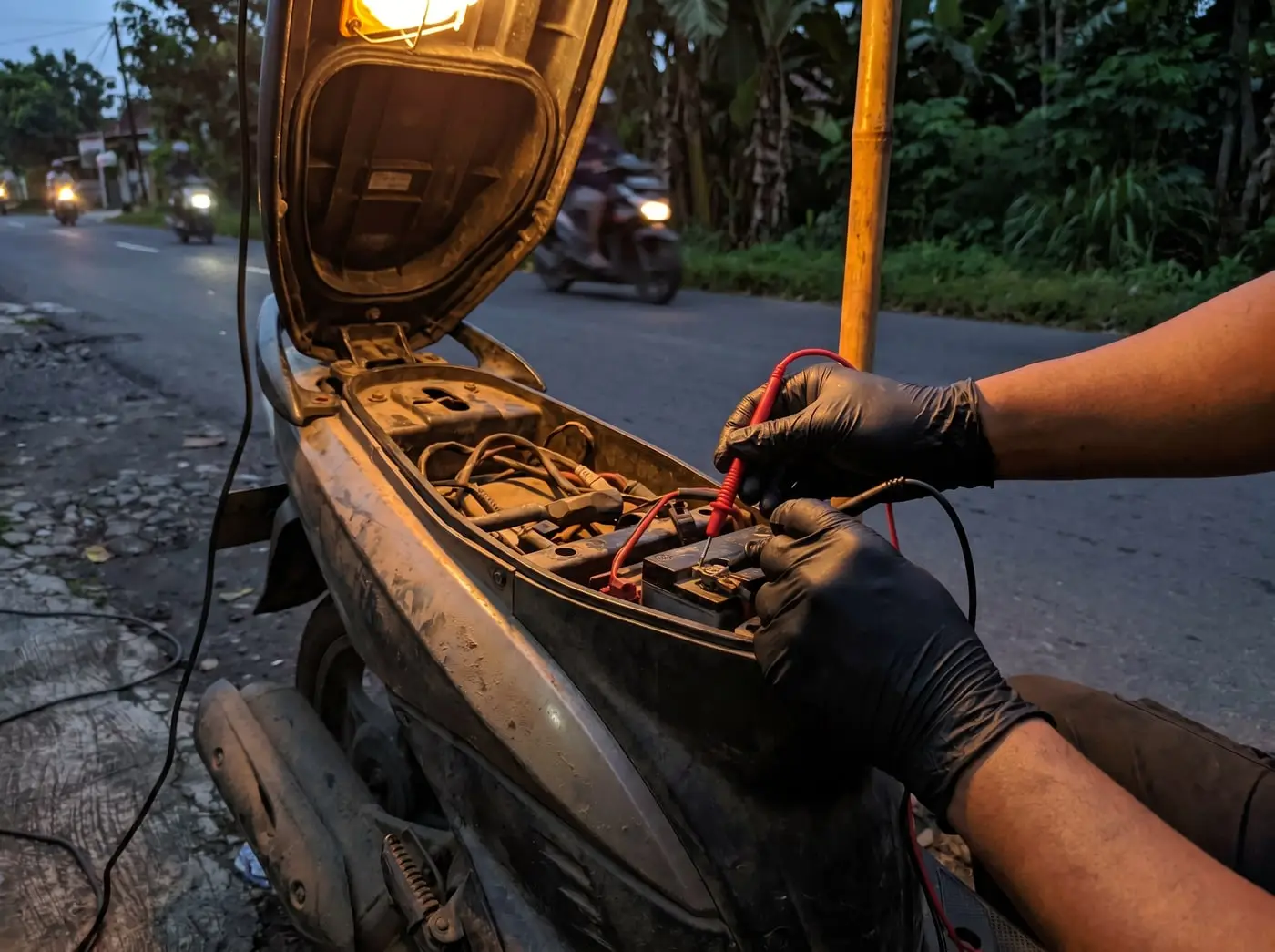 Mekanik MotoCall mengecek aki motor dengan multimeter di lokasi